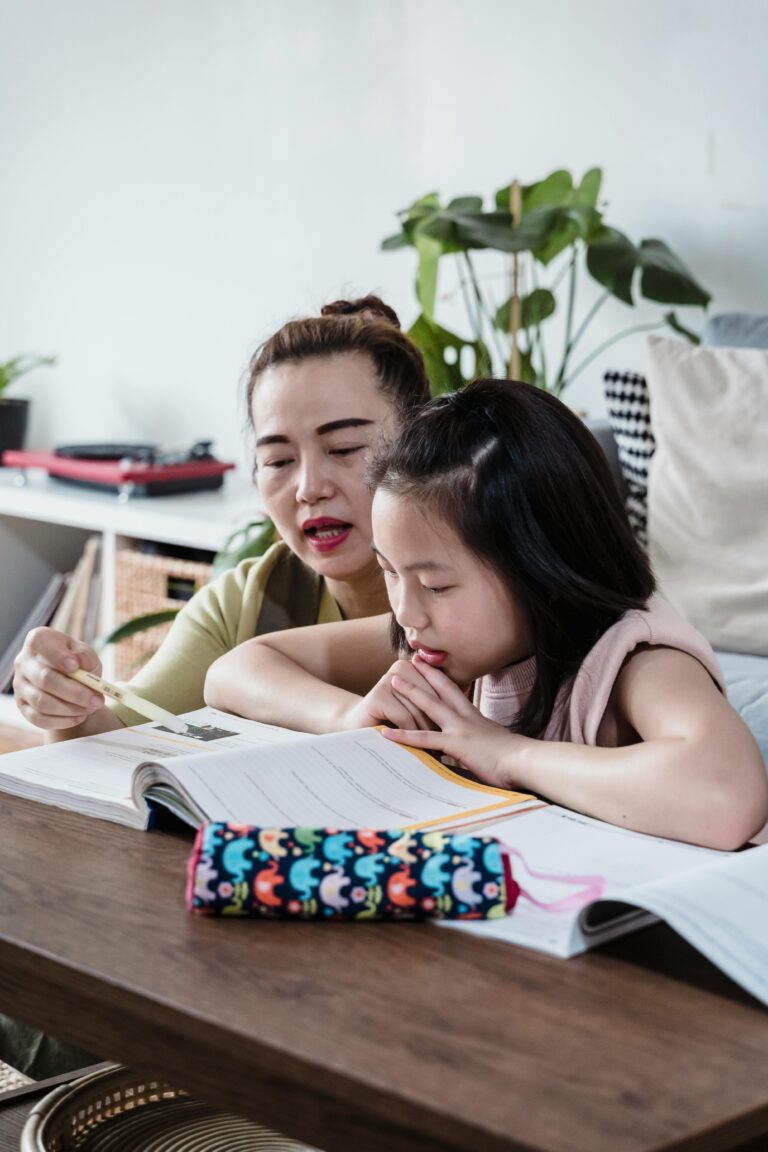 A mother helps her young daughter with homework in a cozy home setting. Ideal for family and education themes.