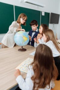 Teacher and students exploring geography with a globe in a classroom setting.